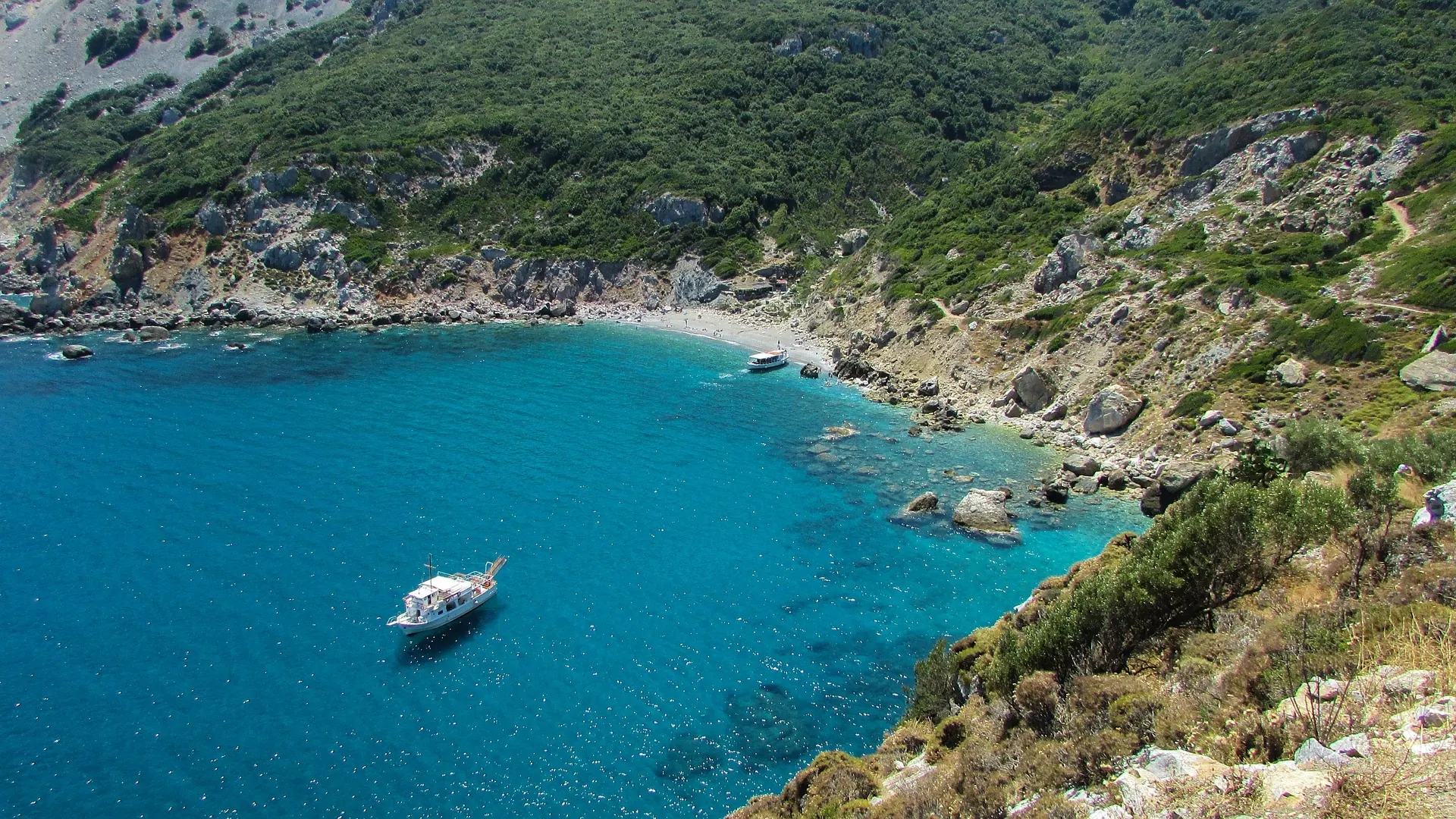 A turquoise cove on the rocky coast of Skiathos, a boat at anchor