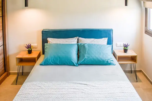 Double bed with teal cushions and a bedside table either side